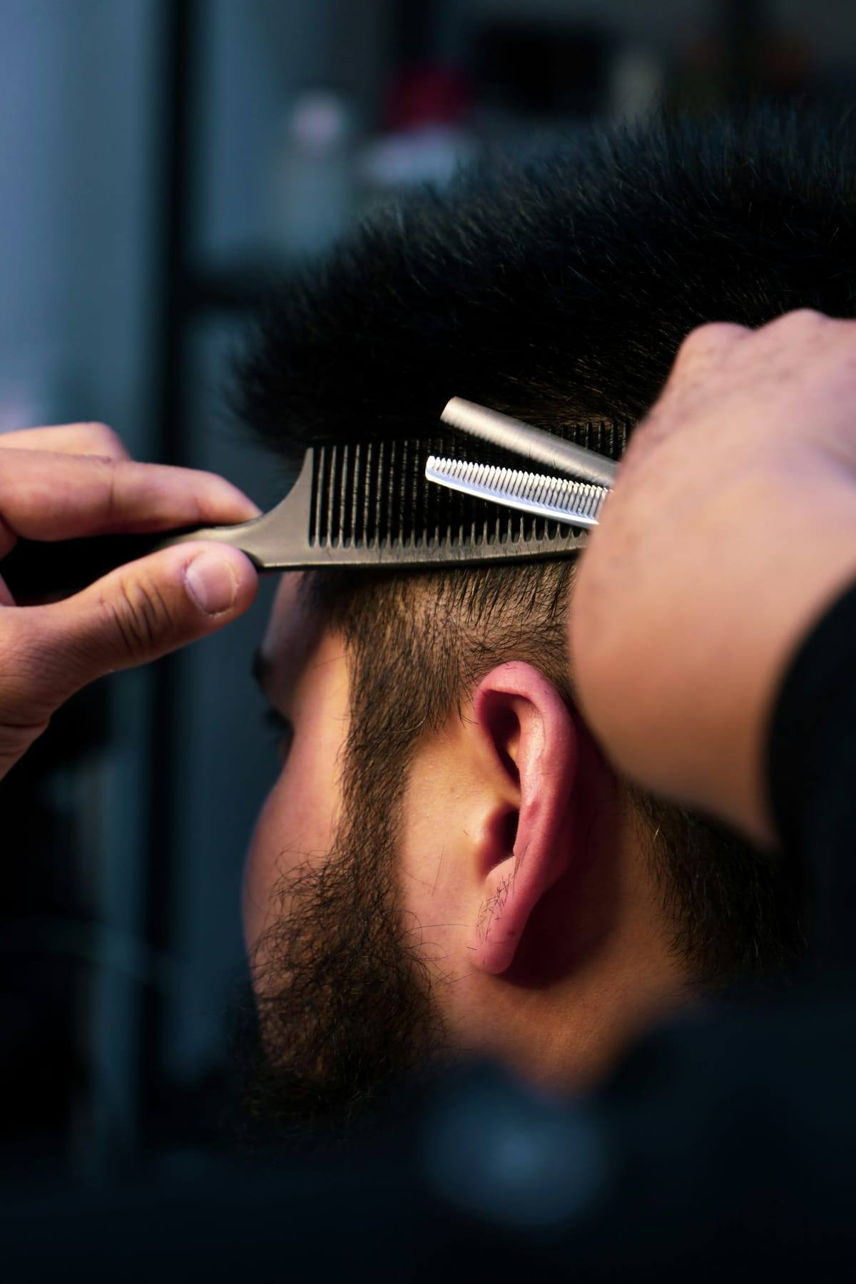 Barber lifting hair with a comb and thinning shears